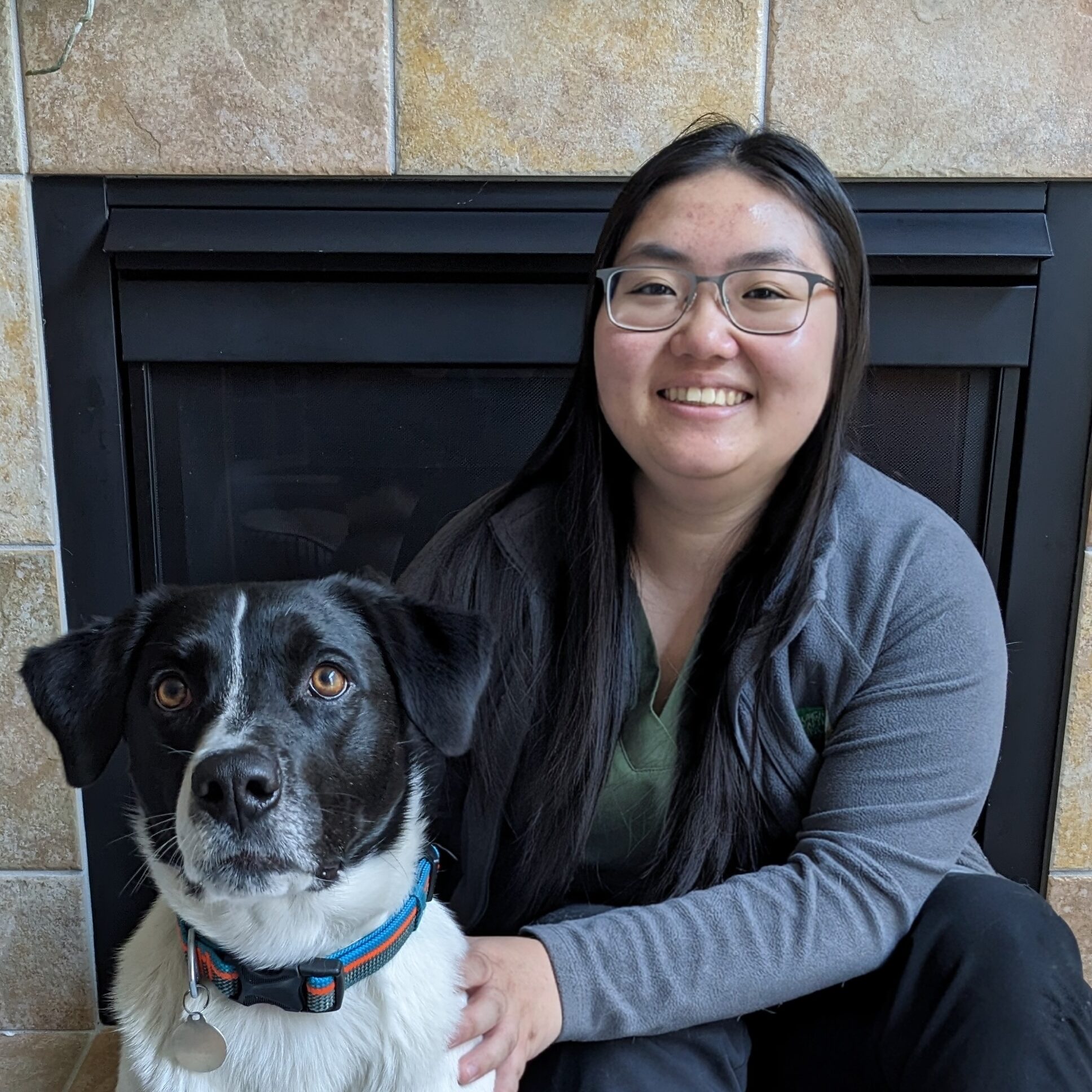 Woman smiling sitting next to a black and white dog.